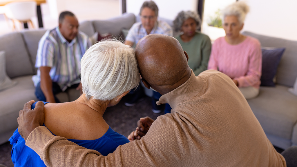 Rear view of senior man lovingly embracing woman in a group with other older adults